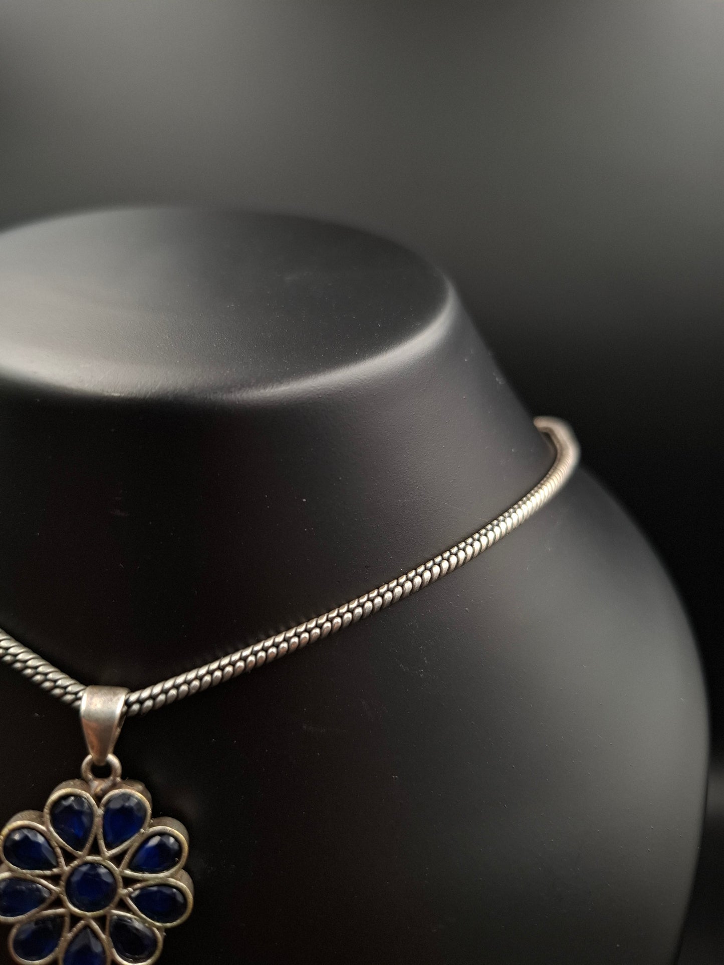 Silver necklace with a blue floral pendant on a black background