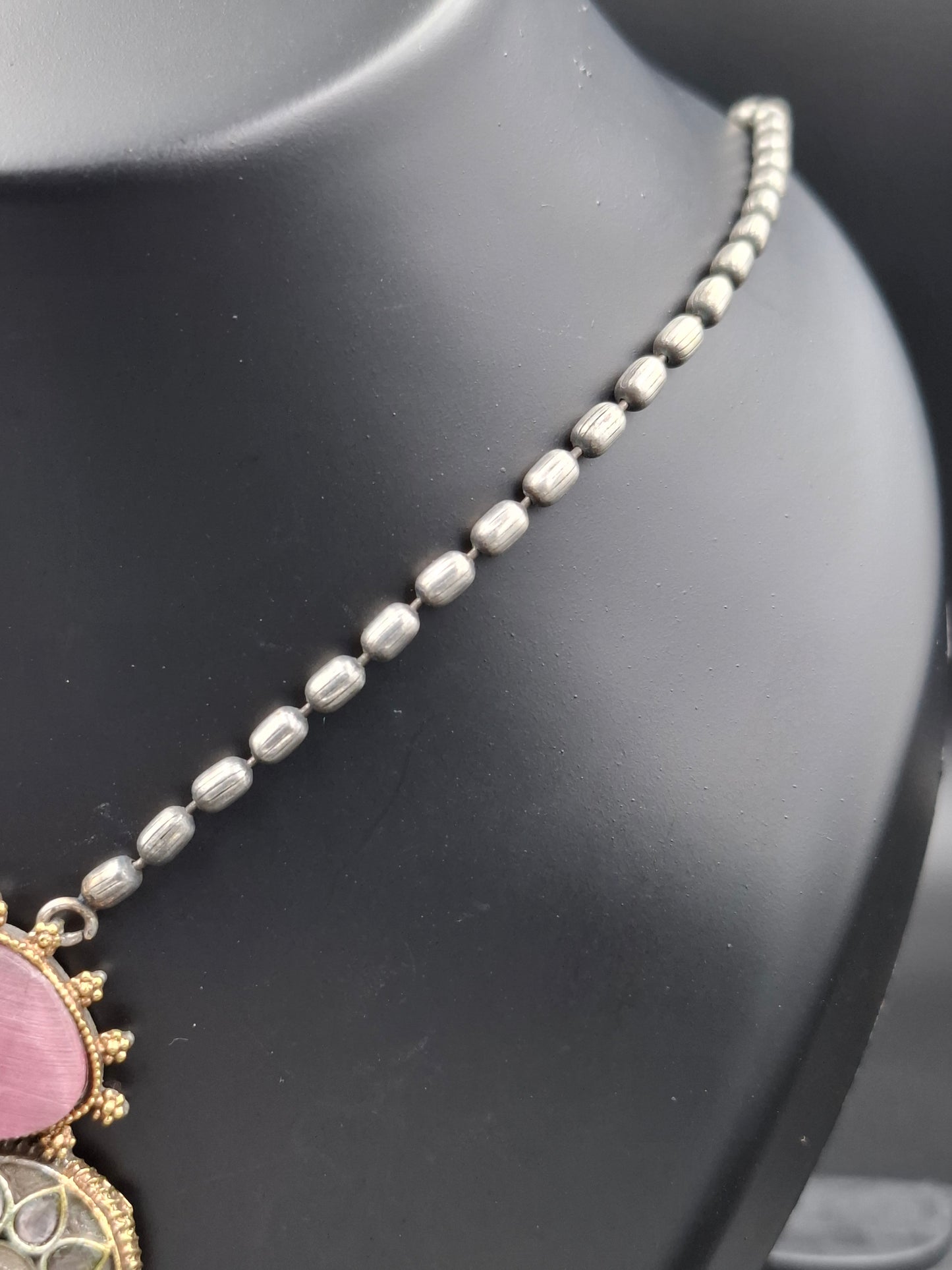 Silver beaded necklace with a pink pendant on a black mannequin bust.
