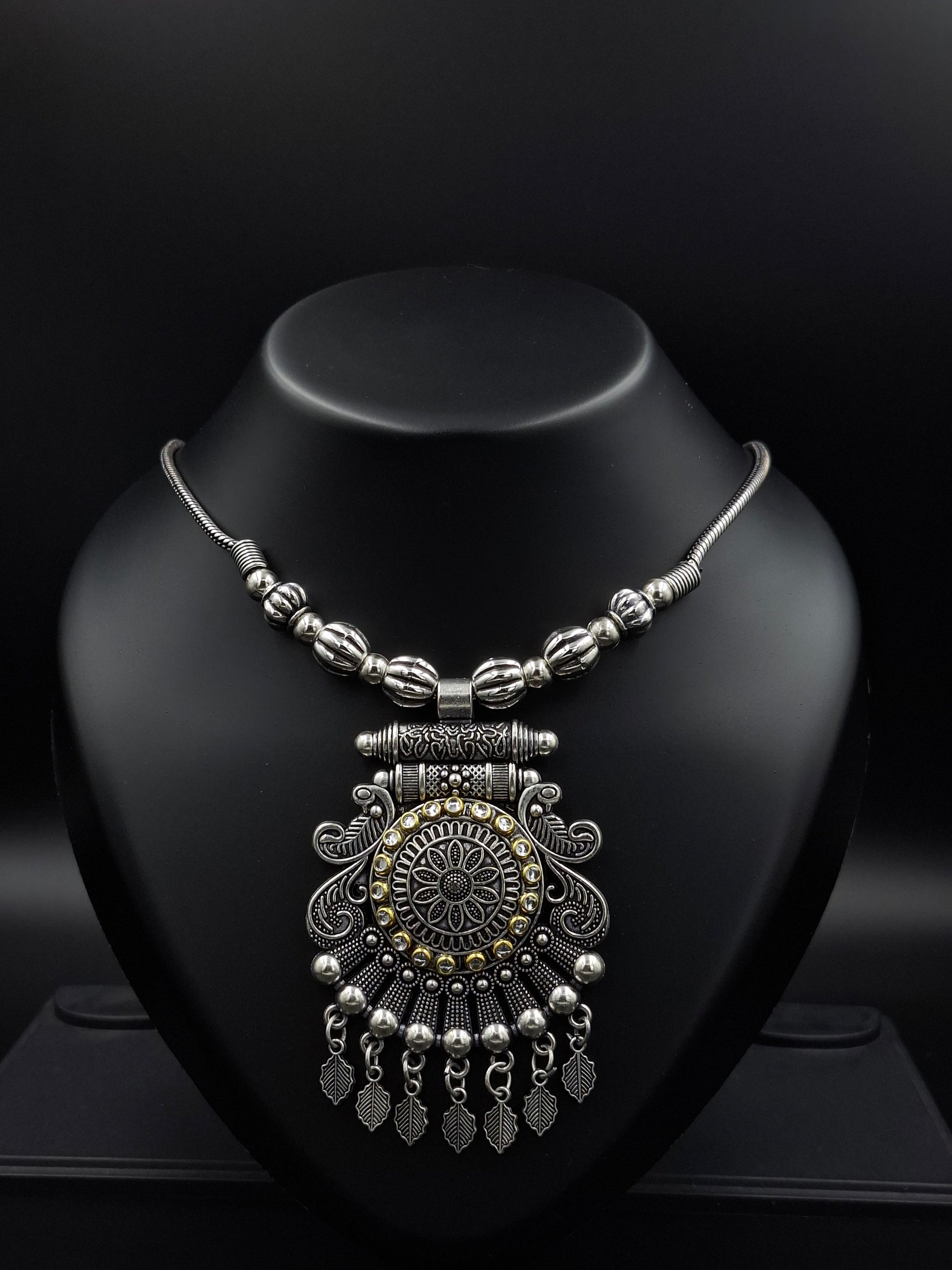 Decorative silver necklace on a black stand with a dark background