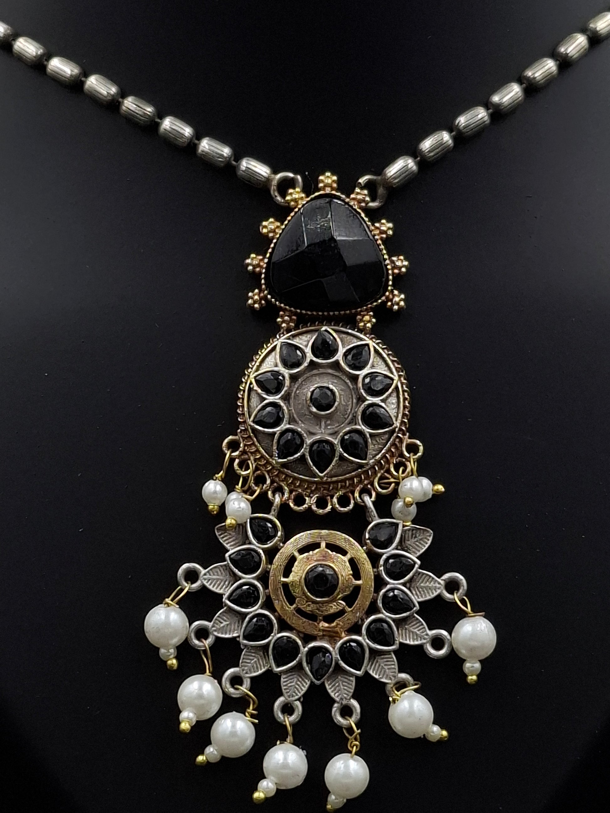 Ornate necklace with black stones, gold accents, and white beads on a dark background