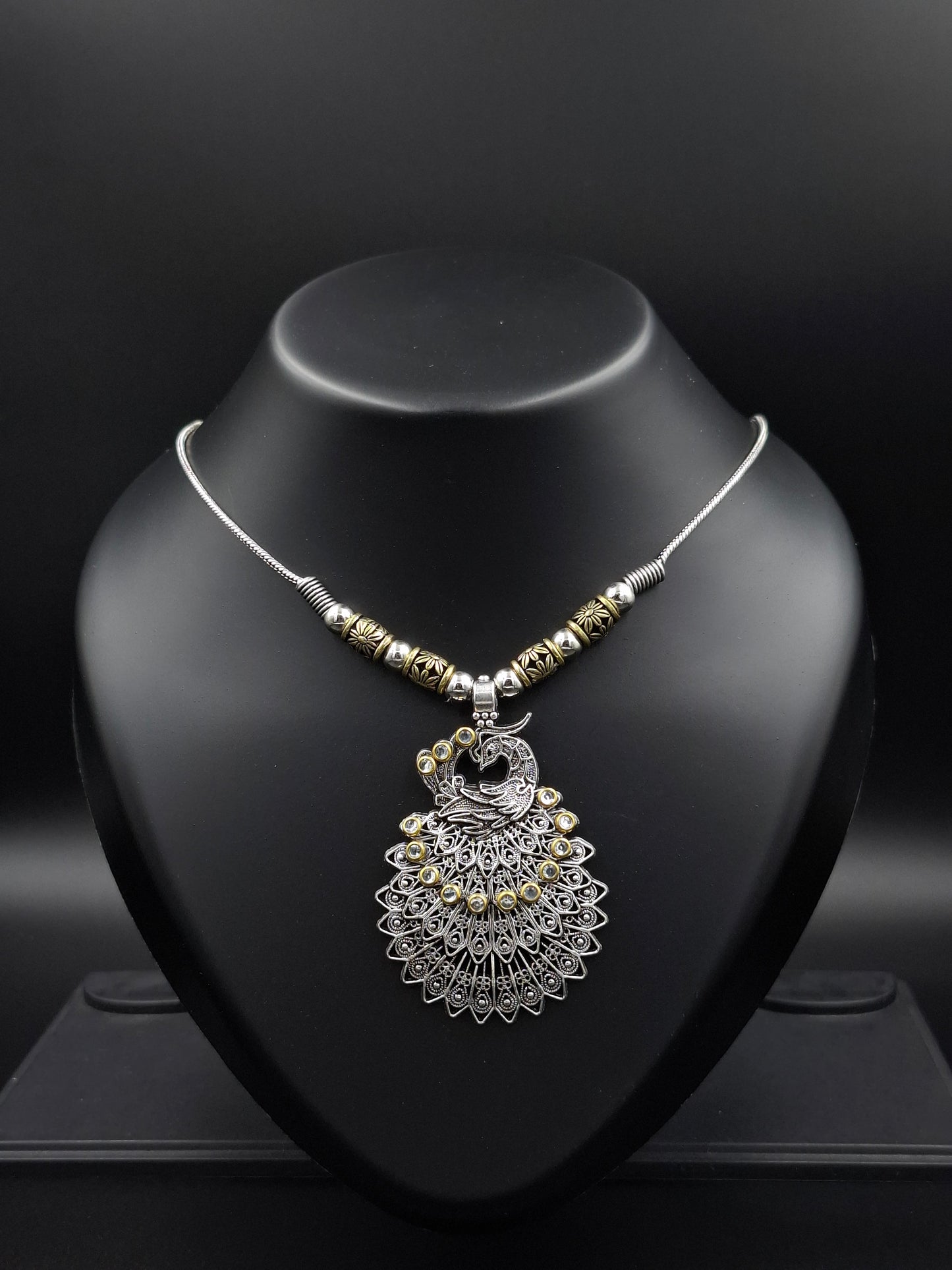 Silver necklace with decorative pendant on a black stand against a dark background