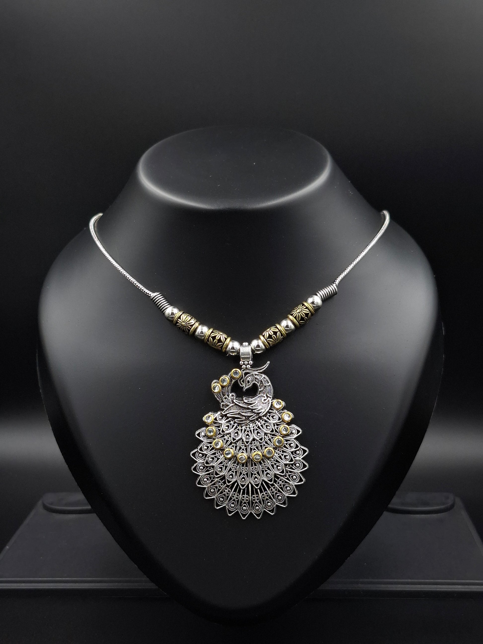 Silver necklace with decorative pendant on a black stand against a dark background