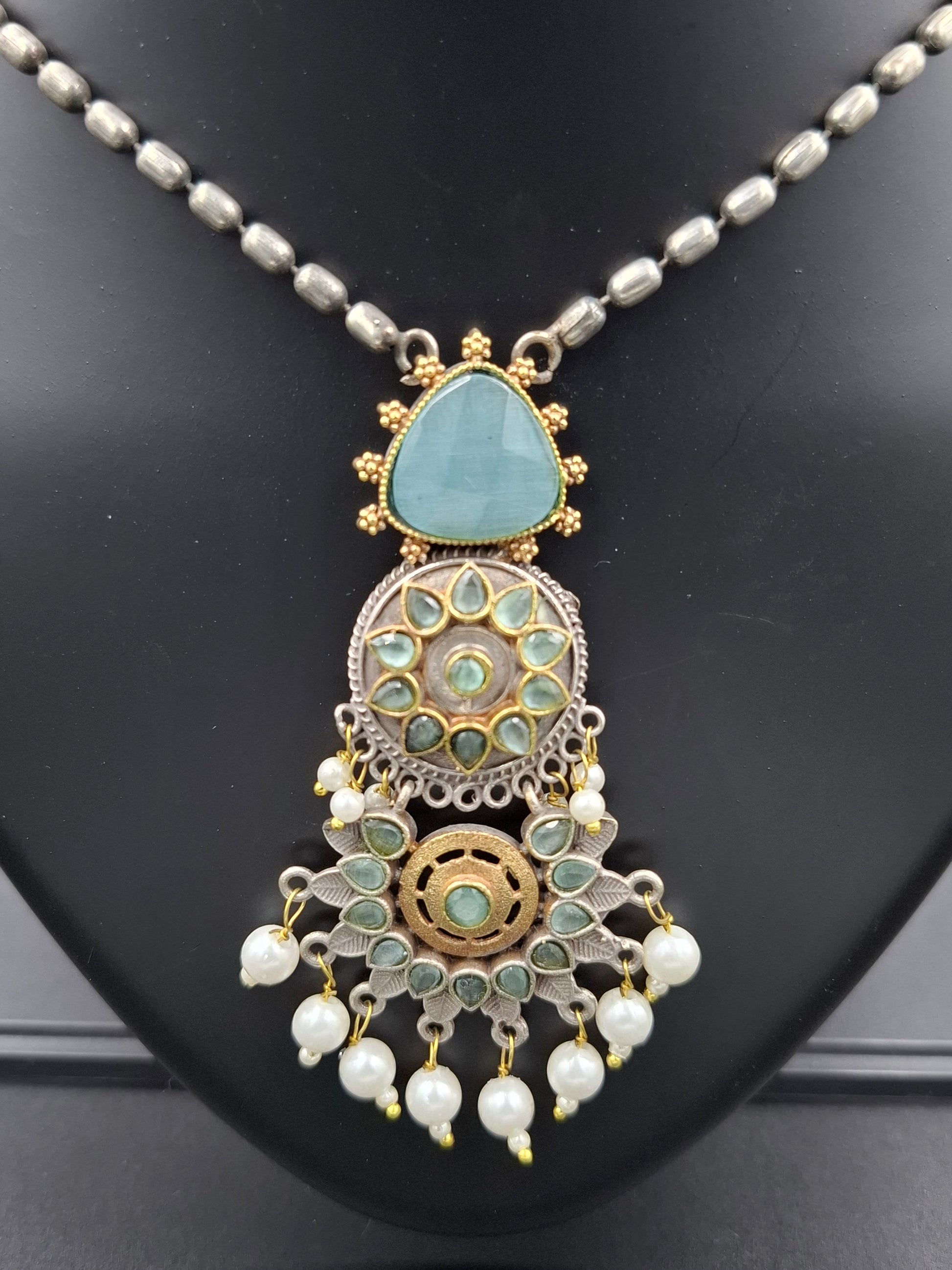Decorative necklace with turquoise stone and pearl-like elements on a black background