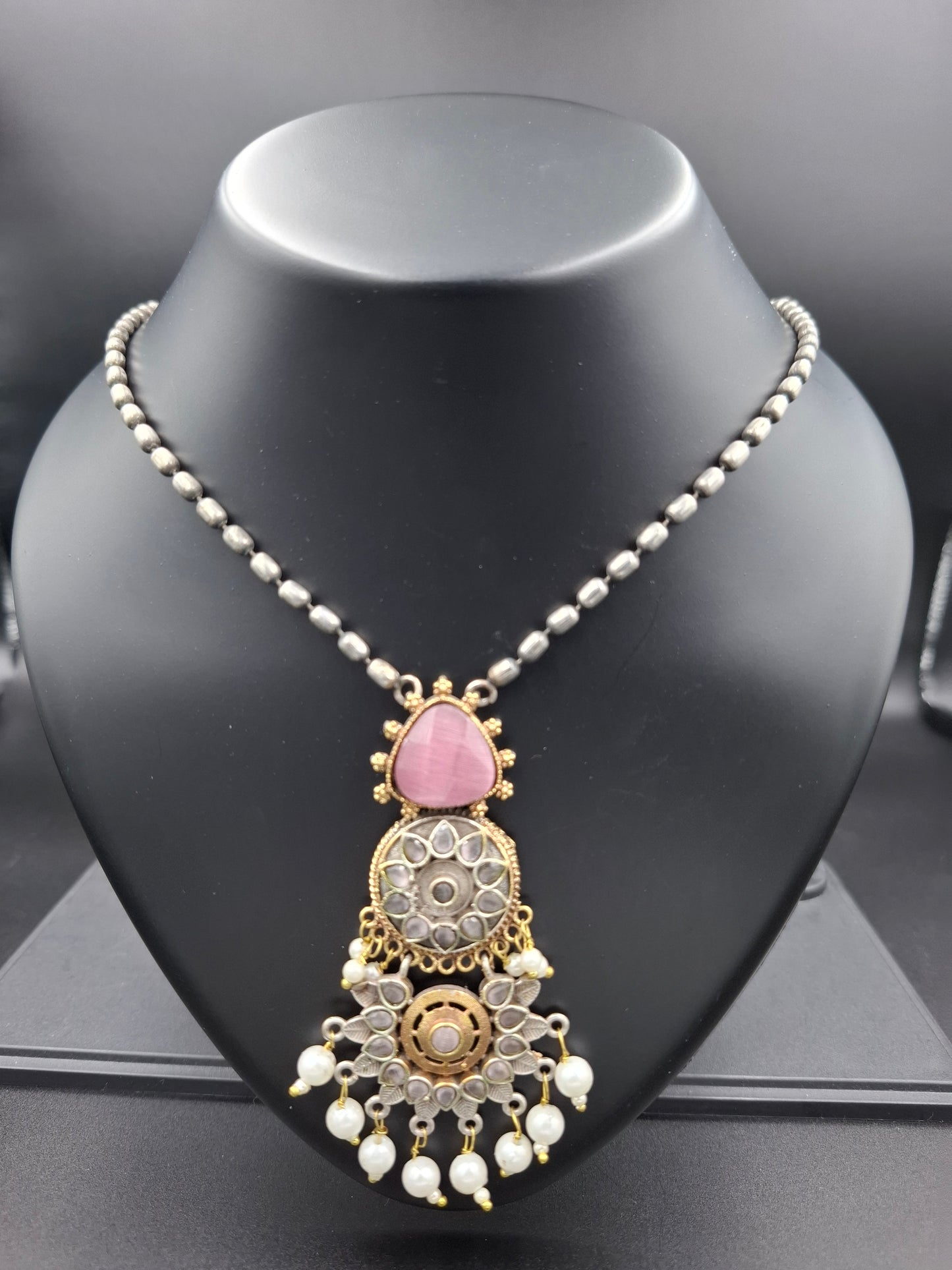 Decorative headpiece with pink gemstone and gold details on a black mannequin head.