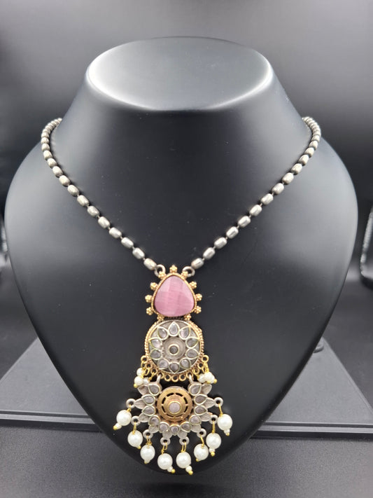 Decorative headpiece with pink gemstone and gold details on a black mannequin head.