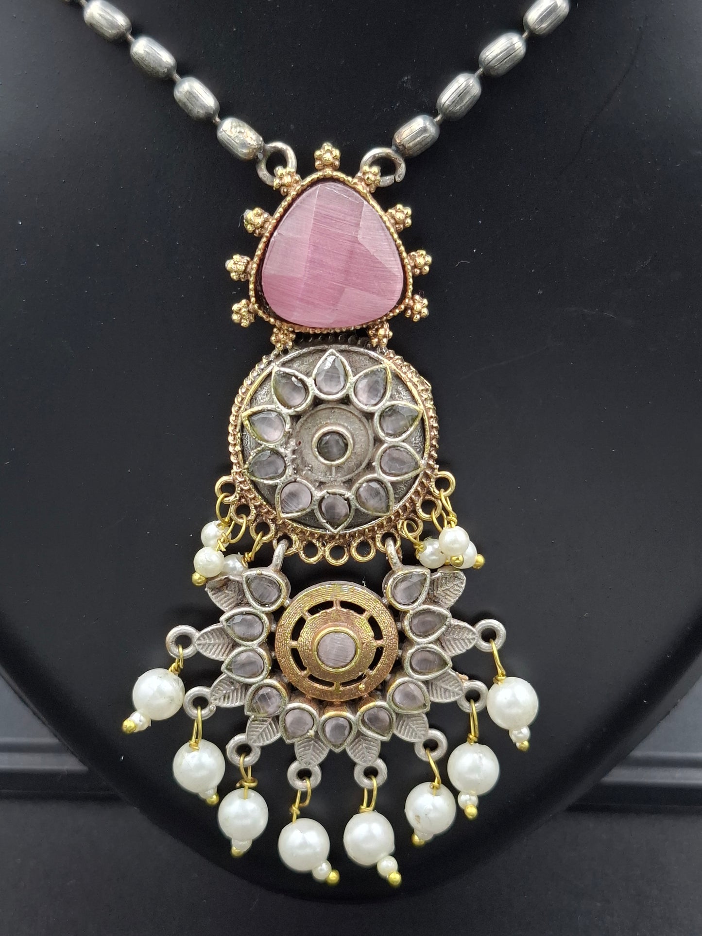Decorative necklace with pink stone and pearl details on a black background