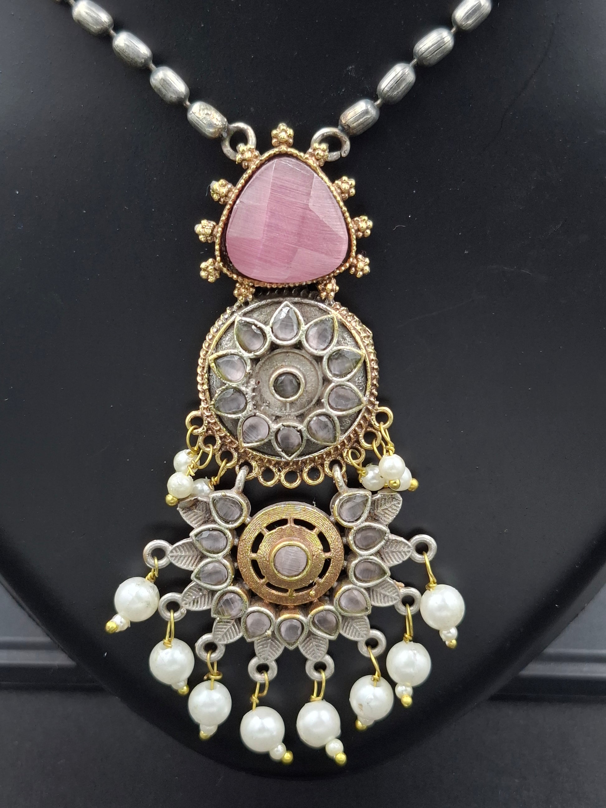 Decorative necklace with pink stone and pearl details on a black background