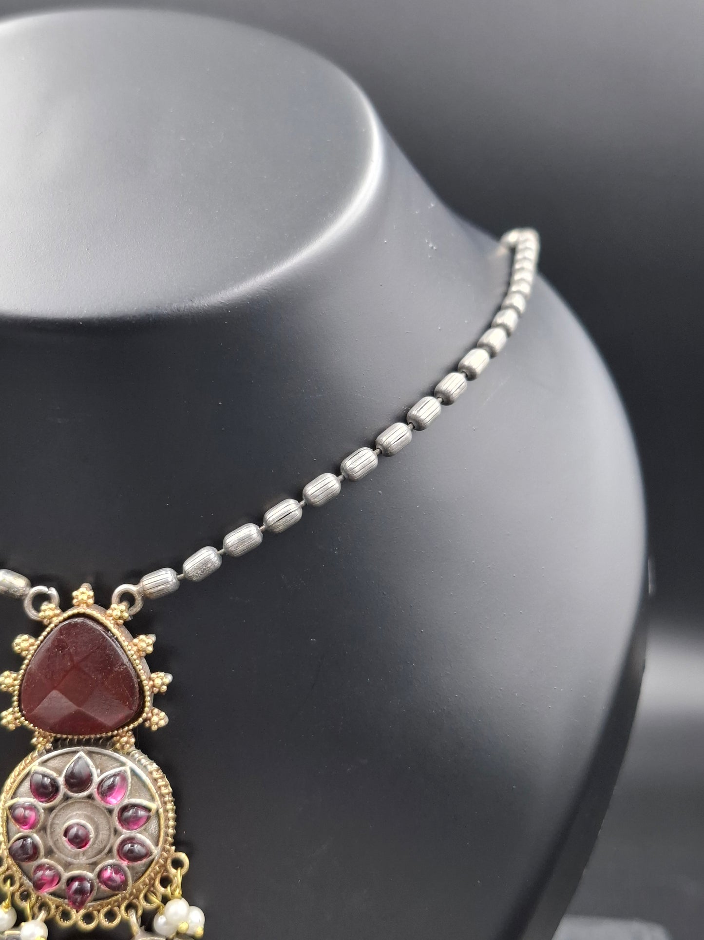Decorative necklace with heart-shaped pendant and gemstones on a black stand.